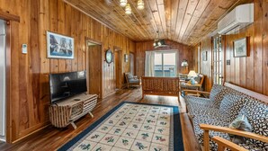 A cozy cabin interior with wooden walls, a television, a patterned sofa, and a large window. - Waterfront Cabin with Inground Pool, Dock, Tennis (Boothbay Harbor)