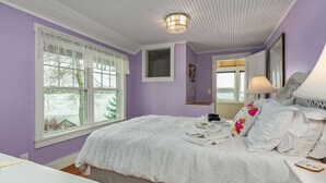 A bedroom with a large bed, a window with white curtains, a bedside table, and a lamp. - Waterfront Cabin with Inground Pool, Dock, Tennis (Boothbay Harbor)