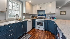 A modern kitchen with dark blue cabinets, white countertops, a built-in oven, and a window providing natural light. - Waterfront Cabin with Inground Pool, Dock, Tennis (Boothbay Harbor)