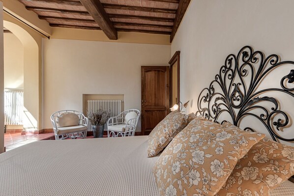 A bedroom with a large bed, white chairs, a wooden door, and a radiator.