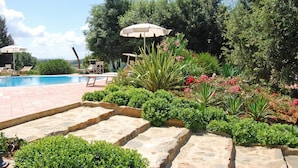 Un espace aménagé au bord de la piscine, avec des marches en pierre menant à la piscine, entouré d’une végétation luxuriante et agrémenté de quelques chaises longues.