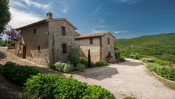 Une maison en pierre avec une allée gravillonnée et une végétation luxuriante.