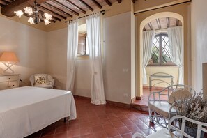 A bedroom with a bed, a nightstand, a chair, a window with curtains, and a view of the outside.