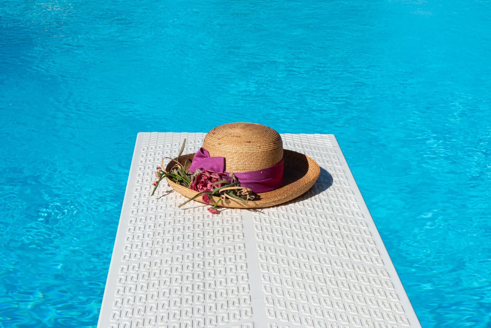 Ambiente piscina con un tappetino bianco strutturato e un cappello di paglia con un nastro rosa.