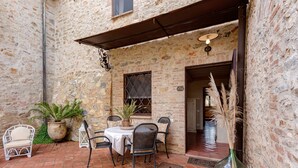 Une terrasse extérieure avec des murs en pierre, une table avec des chaises, des plantes en pot et un luminaire suspendu.