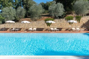 A swimming pool with lounge chairs and umbrellas, surrounded by stone walls and trees.