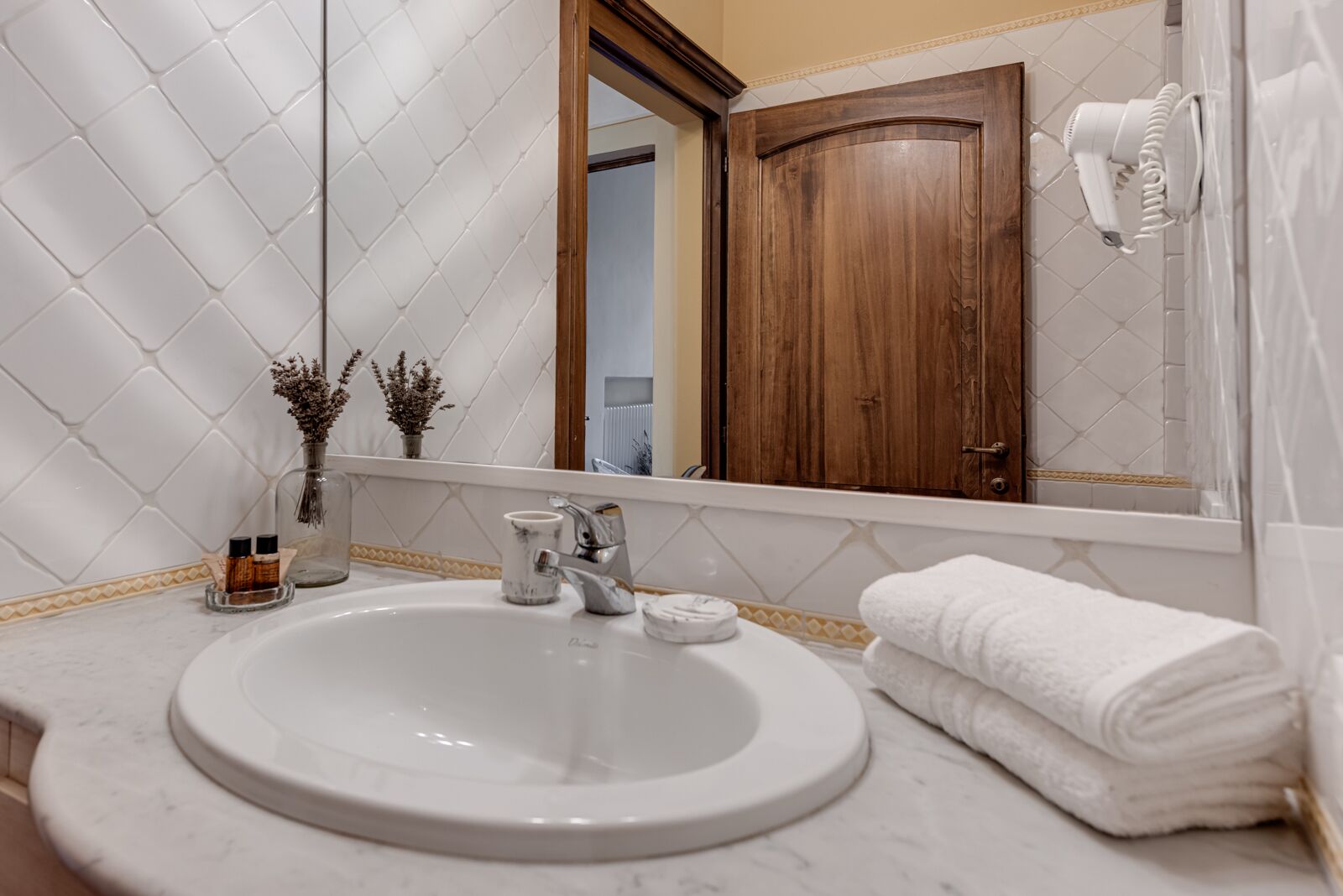 Un baño con un lavabo blanco, una puerta de madera, un espejo y un secador de pelo en la pared.