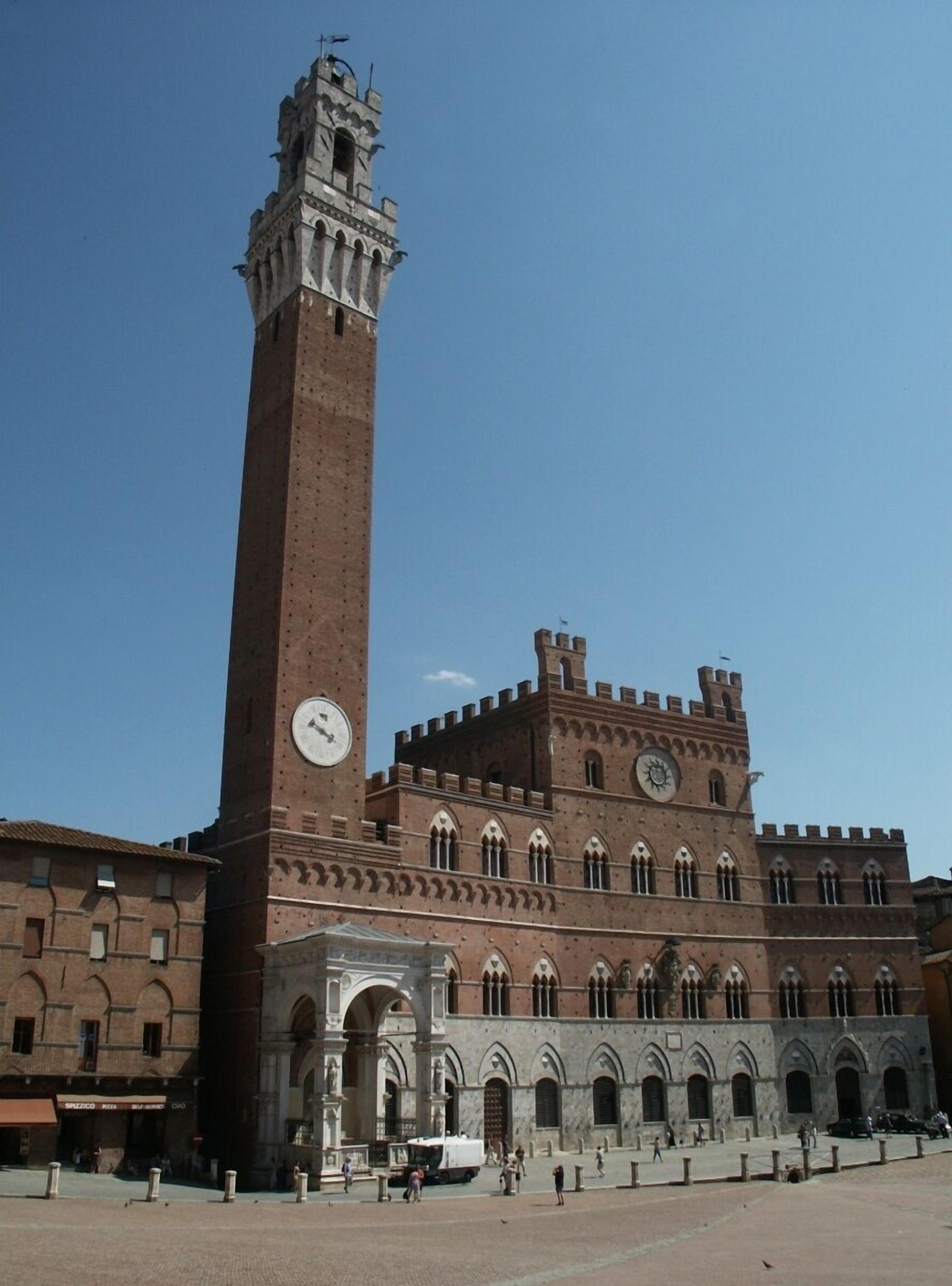 A historic building with a tall clock tower, arched windows, and a central courtyard.