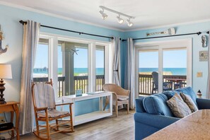 Une pièce avec vue sur la plage, un fauteuil à bascule, un canapé bleu et une table avec une lampe.