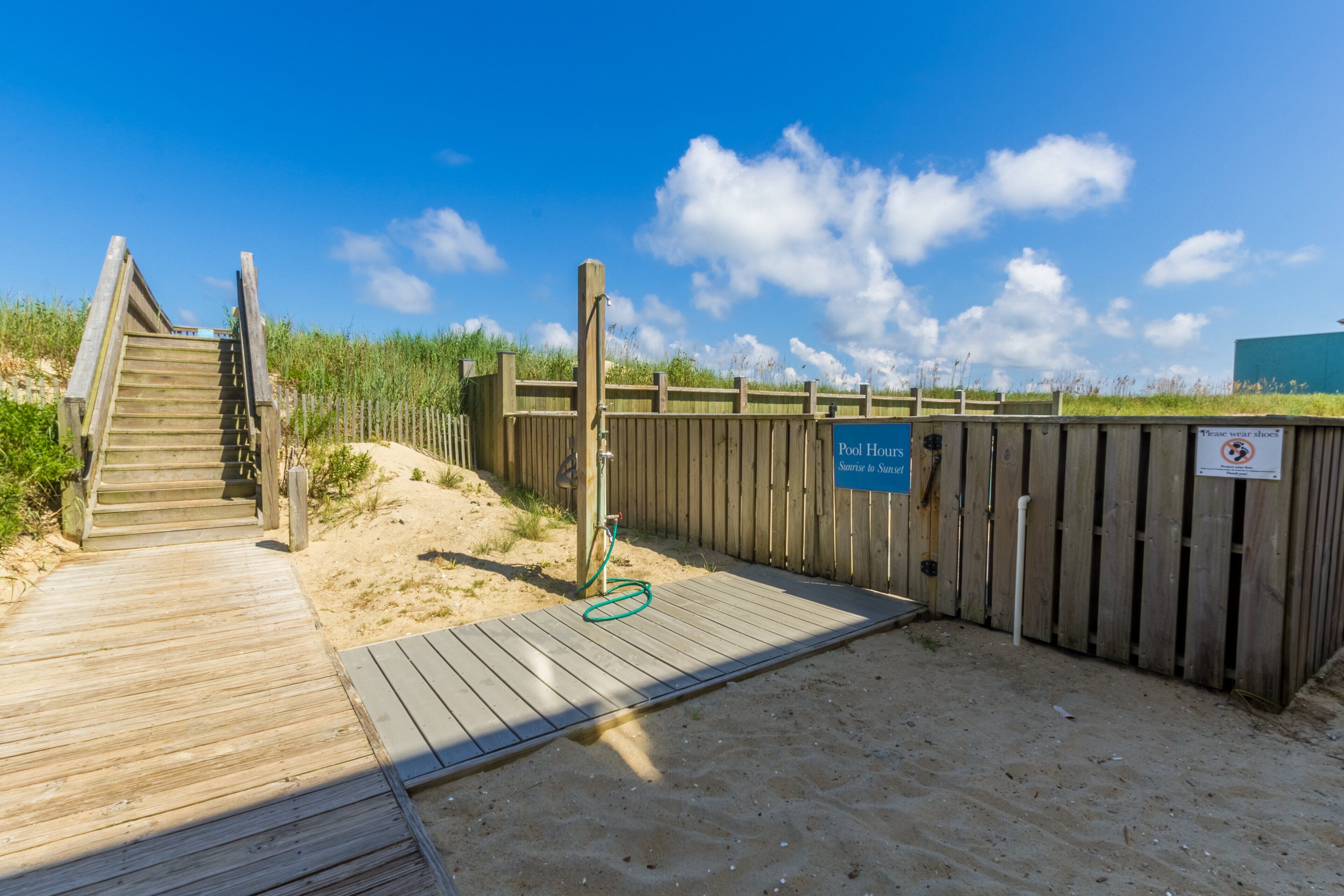 Pasarela de madera que conduce a una zona de playa arenosa, con un cartel que indica 'Horario de la piscina' y un letrero de 'No natación'.