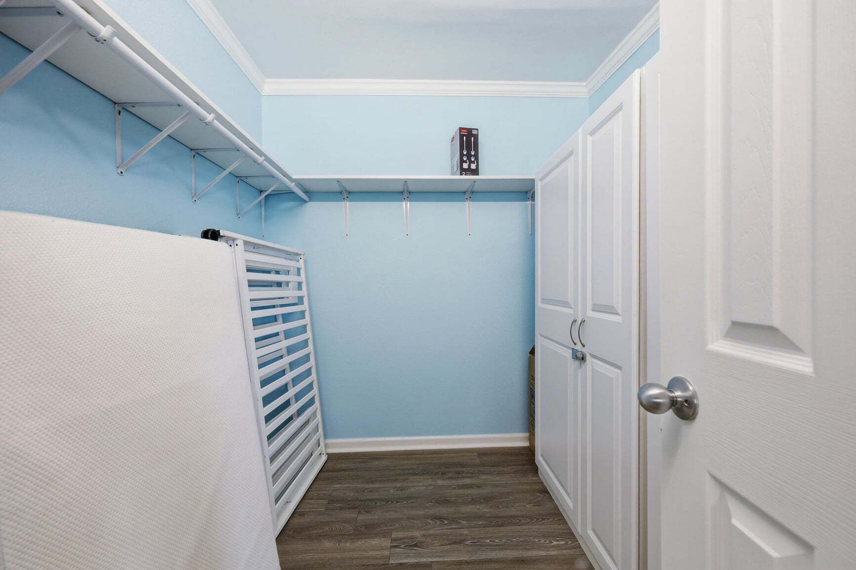 Een smalle gang met een witte radiator, een witte deur en een blauwe muur.
