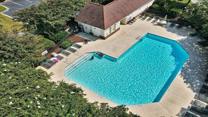 A rectangular swimming pool with a tiled deck surrounding it, a small building with a sloped roof, and a row of sun loungers. - 1024 River Crossing - Barefoot Resort Rentals (North Myrtle Beach)