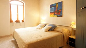 Ein Schlafzimmer mit einem Bett, einem Fenster, einem Gemälde und einem Nachttisch mit einer Lampe.
