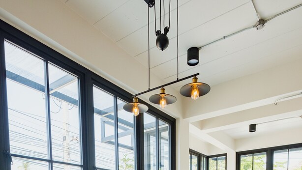 A spacious indoor area with large windows, a wooden table, and yellow and green upholstered seating. - Mosstel (Phitsanulok)