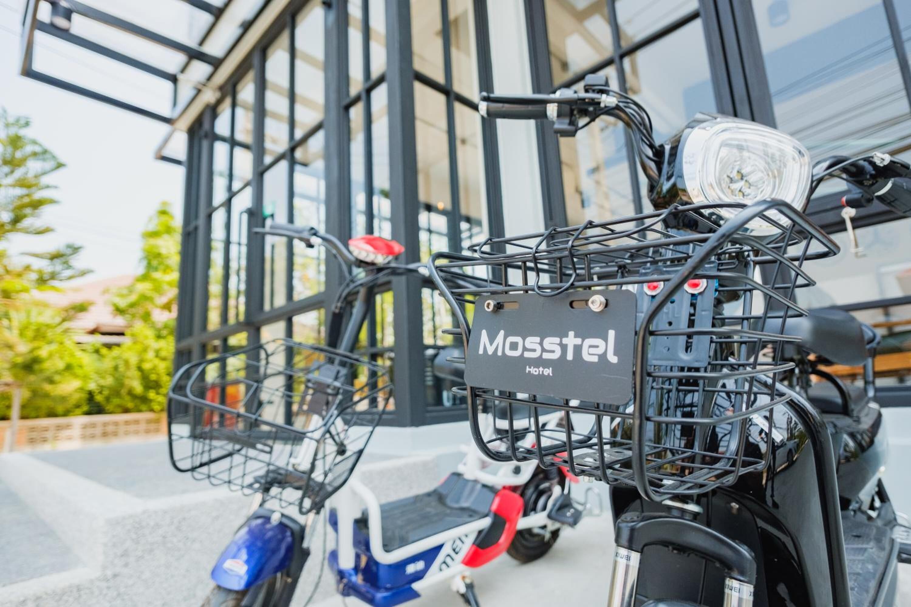Una patineta eléctrica estacionada con una canasta delantera y una etiqueta que dice 'Mosstel Hotel'.