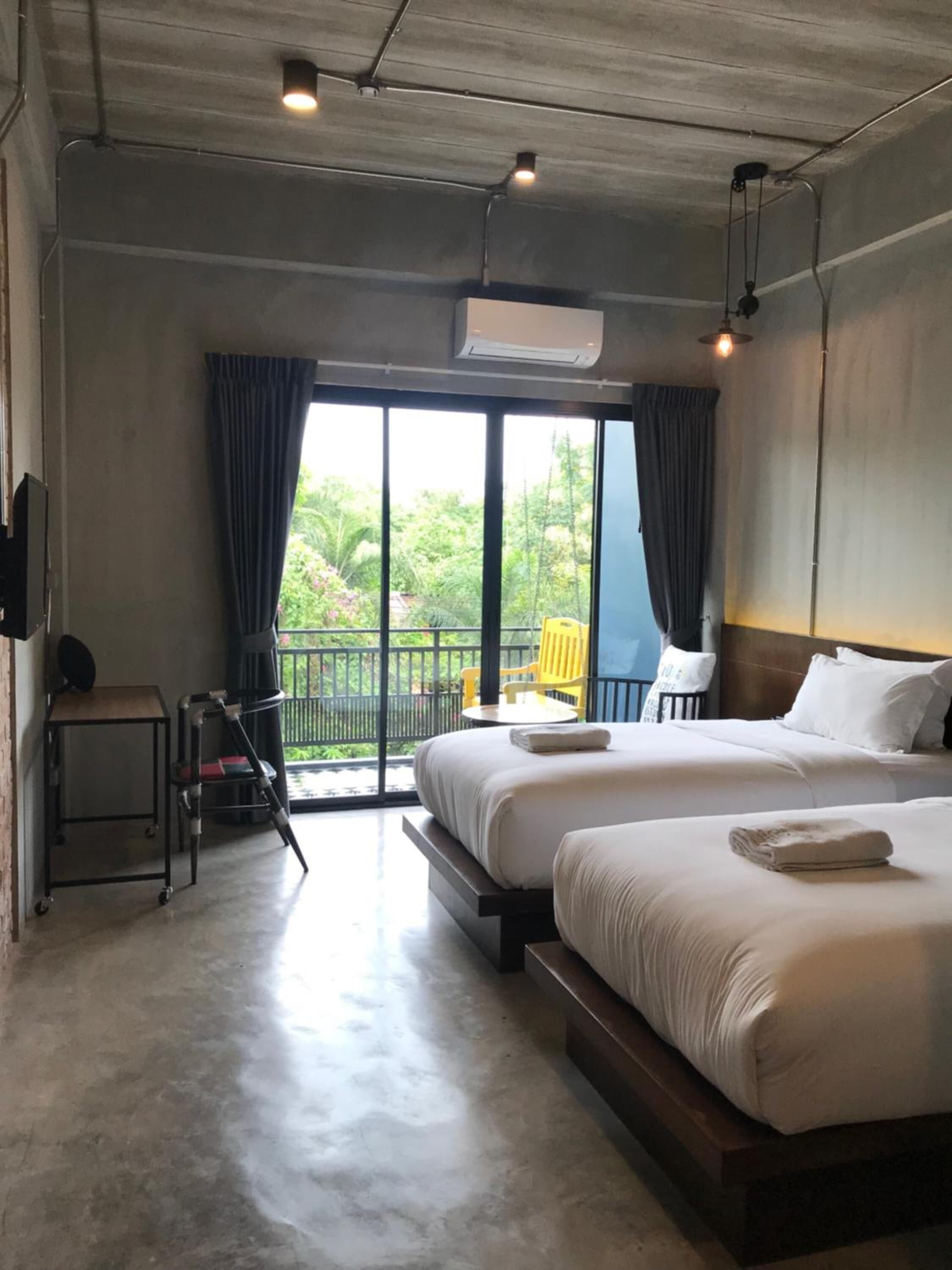 Une chambre d’hôtel avec deux lits, une petite table, une chaise et un balcon donnant sur un espace verdoyant.