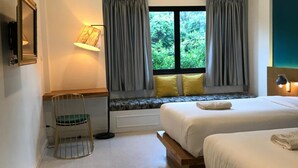 A hotel room with two beds, a desk, a chair, a window with curtains, and an air conditioning unit. - Mosstel (Phitsanulok)
