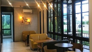 A modern indoor seating area with brick walls, large windows, and a bicycle light decoration. - Mosstel (Phitsanulok)