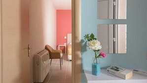 Een hotelkamer met een bed, een stoel, een klein tafeltje en een vaas met bloemen.