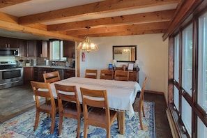 Zona pranzo con tavolo e sedie in legno, un lampadario e vista sulla cucina.