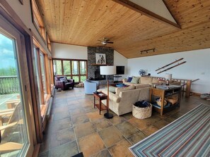 A spacious living area with a stone fireplace, a ceiling fan, and a view of the outdoors. - Sky Ridge - Stunning Mountain Top Views, Hot Tub (Davis)