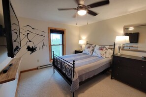 A bedroom with a bed, a ceiling fan, a nightstand with a lamp, a dresser, a mirror, and a window. - Sky Ridge - Stunning Mountain Top Views, Hot Tub (Davis)