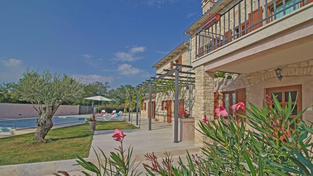 Un espace aménagé au bord de la piscine, avec un bâtiment en pierre, une pergola et une vue sur la piscine.