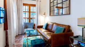 Una sala de estar con un sofá de cuero marrón, una mesa de centro de vidrio, un sillón estampado y un espejo grande en la pared.