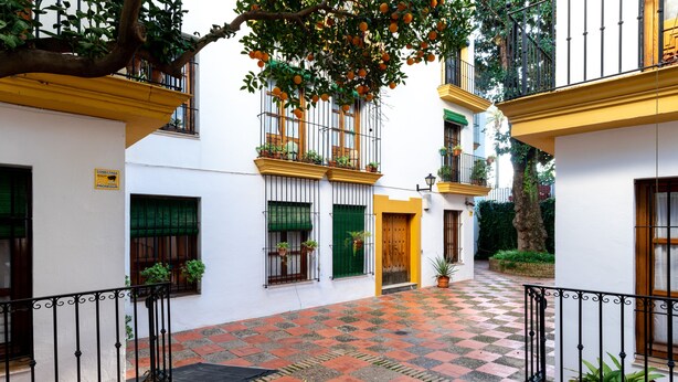 Un patio con piso a cuadros, paredes blancas y balcones con plantas.