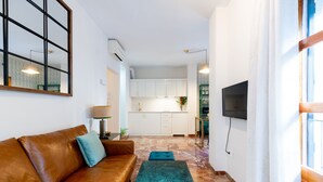 Una sala de estar con un sofá de cuero marrón, un tapete verde azulado y una cocina al fondo.