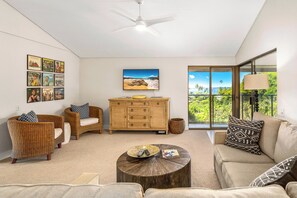 A spacious living room with a large window, a ceiling fan, a wooden cabinet, and a round coffee table.