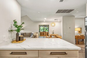 A modern kitchen with a marble countertop, wooden cabinets, and a dining area with a table and chairs.