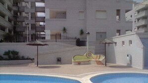 A swimming pool area with two pools, a children's play structure, and a multi-story building in the background. - Perfect views and location (Oropesa)