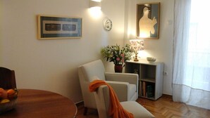 Ein Wohnzimmer mit einem runden Holztisch, einem weißen Sessel, einem Bücherregal und einer Lampe.