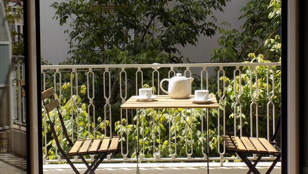 Ein Balkon mit Tisch, gedeckt für Tee, umgeben von Grünpflanzen und einem weißen Geländer.