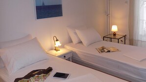 Ein Hotelzimmer mit zwei Betten, einem Nachttisch mit Lampe, einem Segelbootbild und einem Fenster mit Vorhängen.