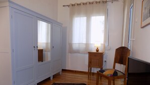 Ein Zimmer mit großem Kleiderschrank, einem kleinen Nachttisch mit Lampe, einem Sessel und einem Fernseher.