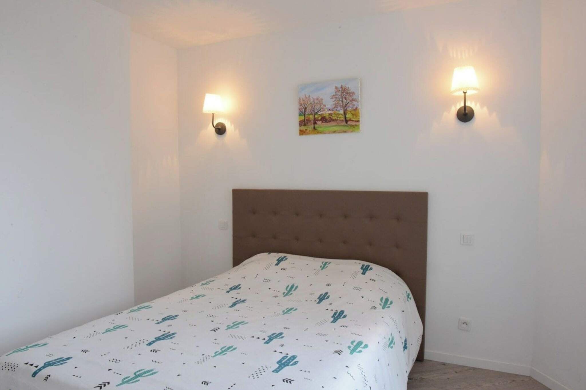 Une chambre à coucher avec un lit, deux lampes fixées au mur et un tableau accroché au mur.