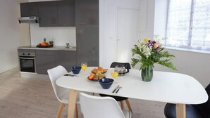 A modern kitchen with grey cabinets, a built-in oven, and a dining area with a white table and chairs. - Perle Marine - Dieppe (Dieppe)