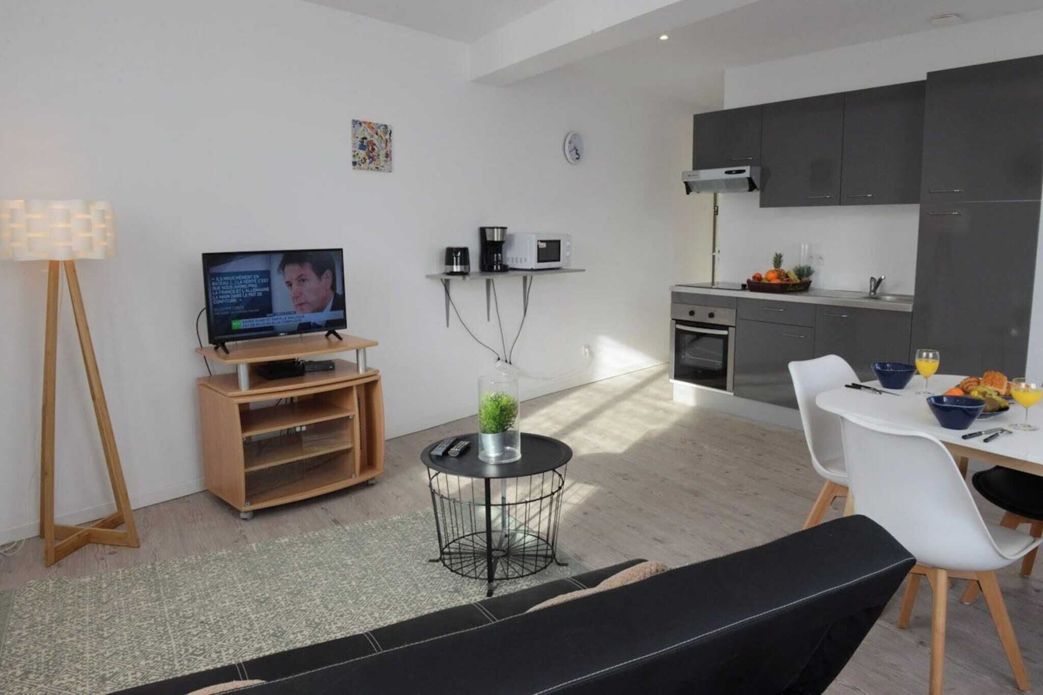 Un salon moderne comprenant un téléviseur, une petite table ronde avec une plante, un canapé et un coin repas avec une table et des chaises.