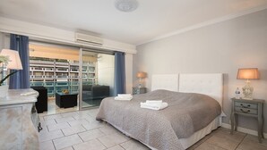 Un dormitorio con una cama grande, un escritorio y una silla. Hay una puerta corrediza de vidrio que da a un balcón con vistas a la ciudad.