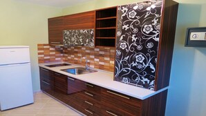 Une cuisine équipée d’un réfrigérateur encastré, d’un évier à deux bacs, de meubles de rangement en bois et d’un crédence décorée de carreaux à motifs.