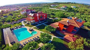 Vue aérienne d’un quartier résidentiel avec une grande piscine, plusieurs maisons et une végétation luxuriante.