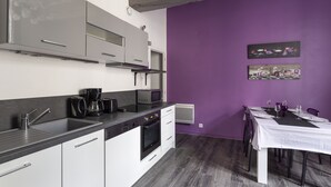 Une cuisine équipée d’appareils électroménagers modernes, un coin repas avec une table dressée pour quatre personnes, et un mur d’accent de couleur violette.