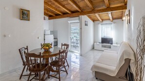 Uma área de refeições com uma mesa e cadeiras de madeira, uma cesta de frutas e uma cozinha ao fundo.