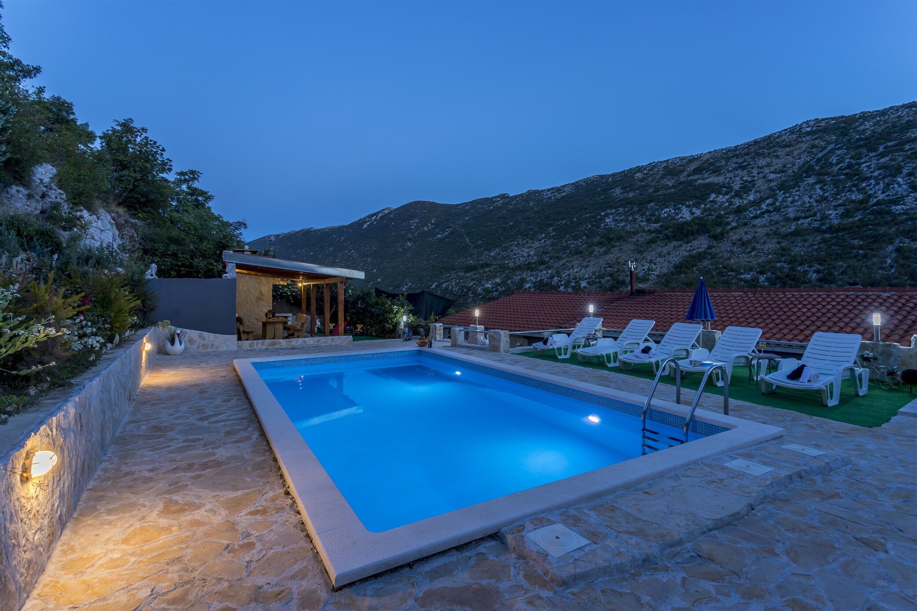A rectangular swimming pool with a stone border, surrounded by lounge chairs and a small bar area.