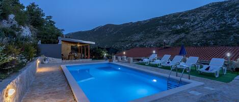 A rectangular swimming pool with a stone border, surrounded by lounge chairs and a small bar area.