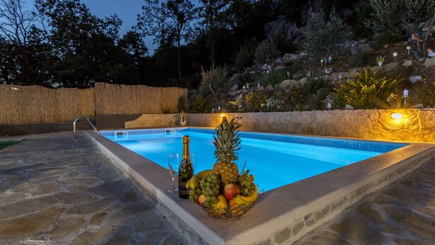 Piscina com borda de pedra, cesta de frutas e uma garrafa de champanhe.