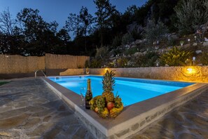 Ein Schwimmbecken mit Steinumrandung, eine Obstkorb und eine Champagnerflasche.