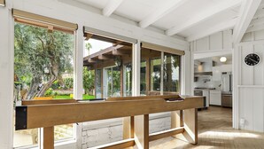 A modern kitchen with white cabinetry, a wooden bench, and large windows overlooking a garden. - Luxury Palm Desert Mid-Century Home Private Pool Golf Course (Palm Desert)